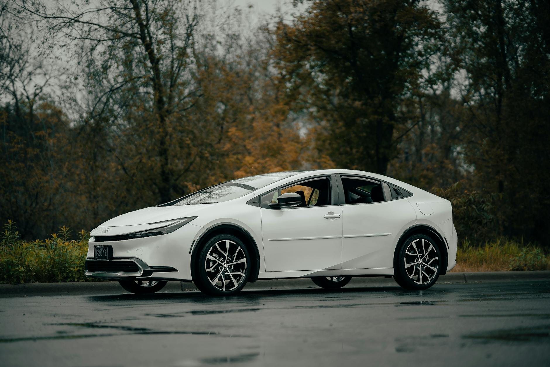 Czy warto kupić Toyotę z hybrydą? Fakty i mity po latach użytkowania Biała Toyota sedan z boku na mokrej drodze w jesiennym otoczeniu