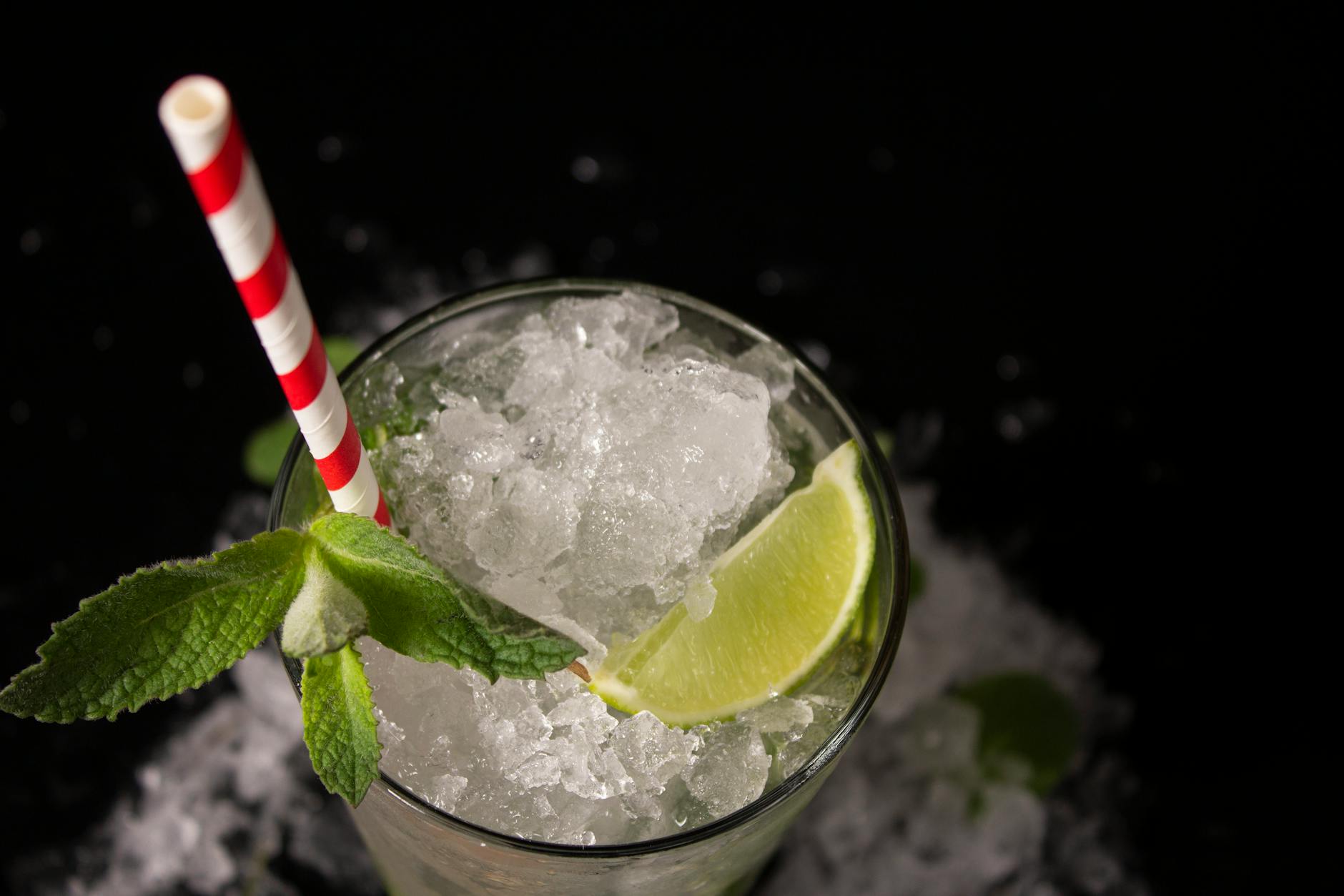Koktajl mojito z limonką, miętą i słomką na czarnym tle